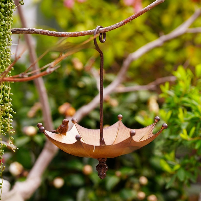 Bronze-Vogelfutterer im Schirm-Design hängt an einem Ast im grünen Garten zwischen Blättern
