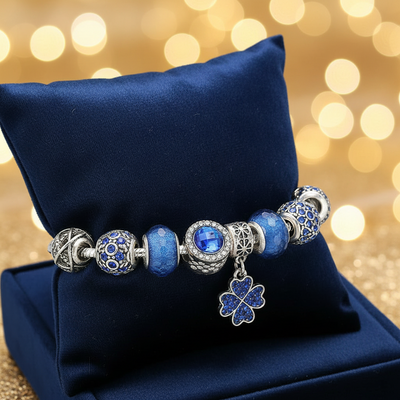Charm-Armband Blau mit Kleeblatt-Anhänger, blauen Kristallperlen und Glasperlen auf dunkelblauem Samtkissen