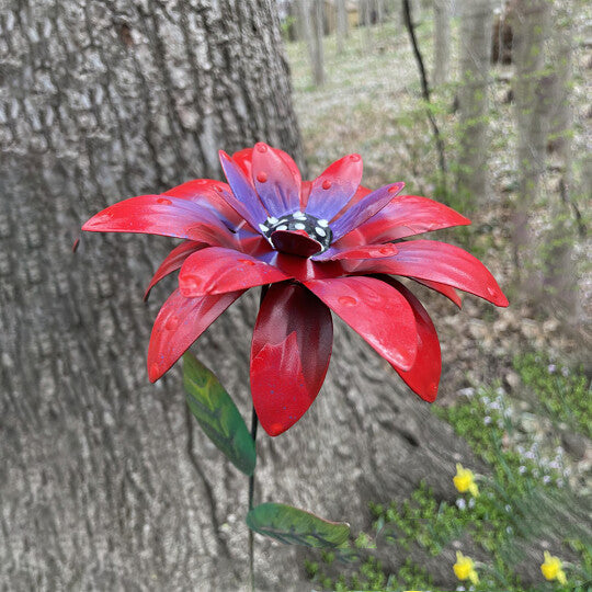 Roter Blumenstecker Metall aus Schmiedeeisen zwischen blühenden Rosen im Garten