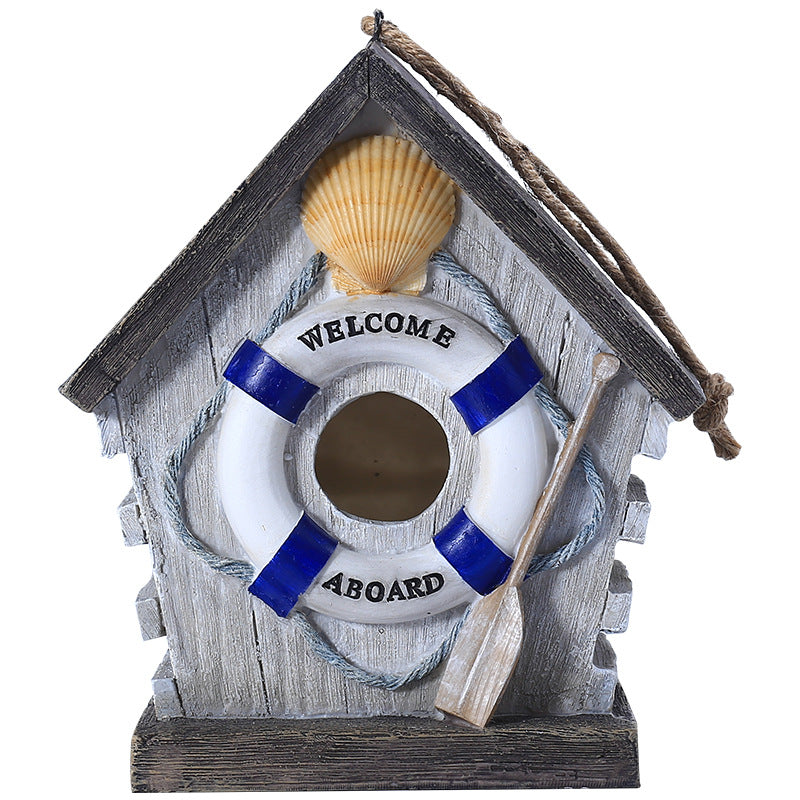 Maritimes Vogelhaus mit Welcome-Aboard-Rettungsring und Paddel auf dunklem Sockel