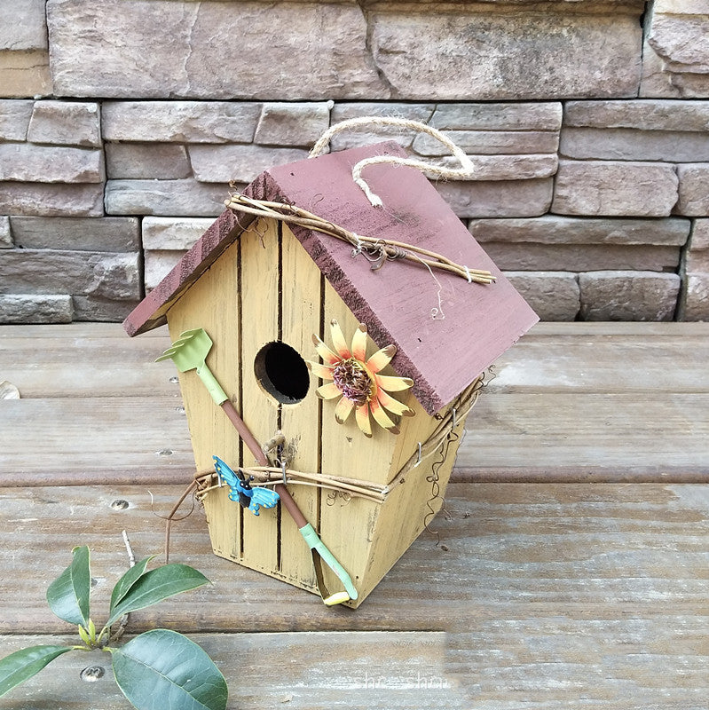 Gelbes Vogelhaus aus Holz mit rosa Dach, Sonnenblume und Libelle als Gartendeko