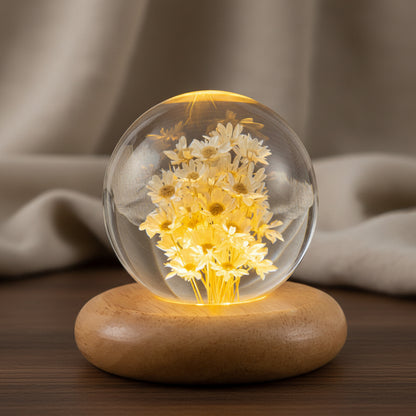 Cremegelbe Margeriten in einer 7 cm Kugel aus Kunstharz auf flachem, abgerundetem Holzsockel vor hellem Stoff
