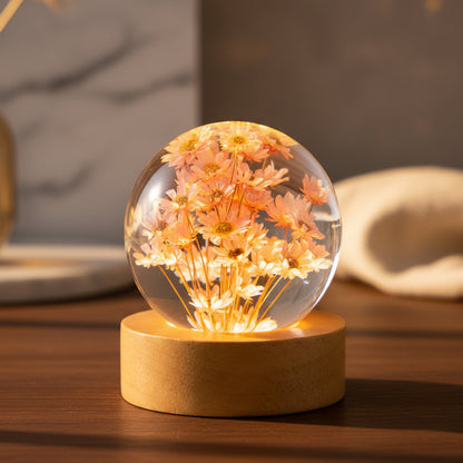 Kleine Nachttischlampe mit rosa Margeriten in einer 6 cm Kugel aus klarem Kunstharz auf rundem Holzsockel